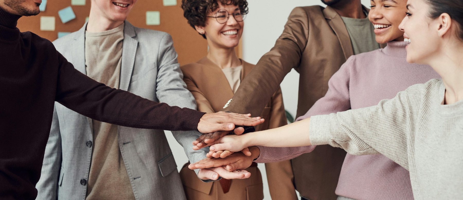 Equipo diverso colocando sus manos al centro como símbolo de colaboración e inclusión
